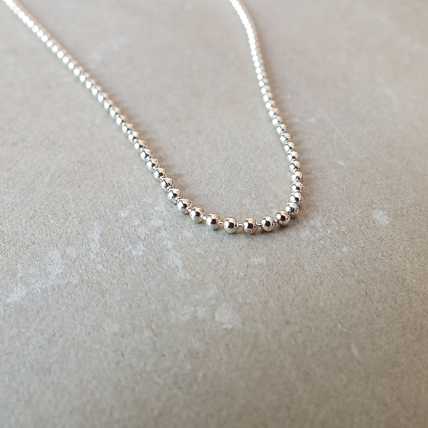 Close-up of the Becoming Jewelry Bead Chain Necklace laid out flat on a light-colored surface, showcasing its intricate silver texture.