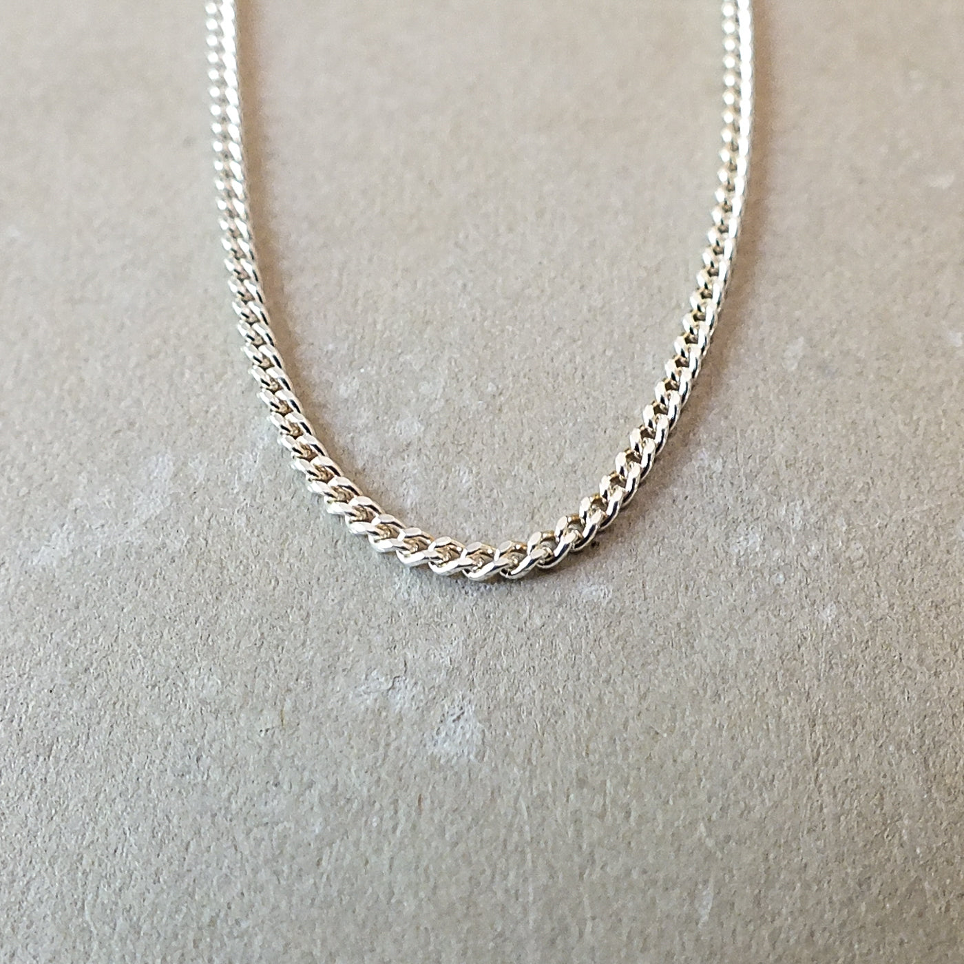 Close-up image of Becoming Jewelry&#39;s delicate Curb Chain Necklace in silver, elegantly placed on a beige surface—ideal for layering with other classic Curb Chain pieces.