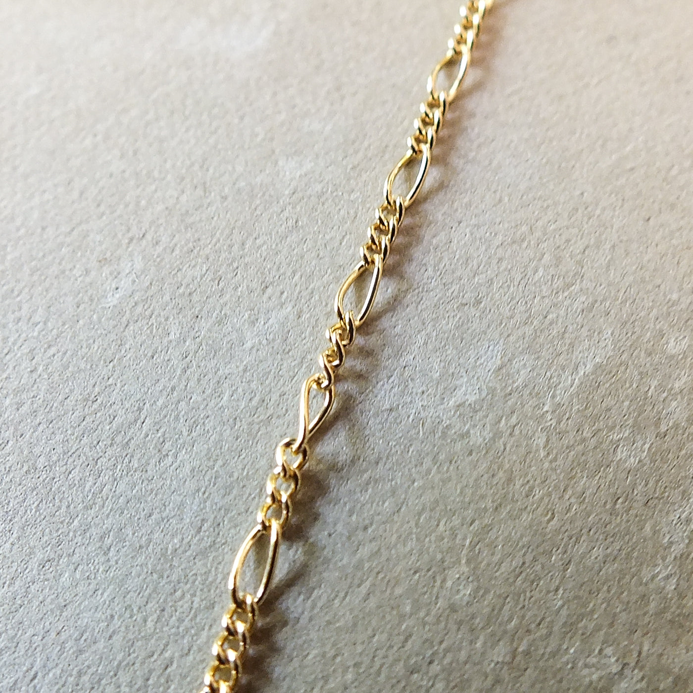 Gold filled Becoming Jewelry Figaro Chain Necklace on a textured surface.