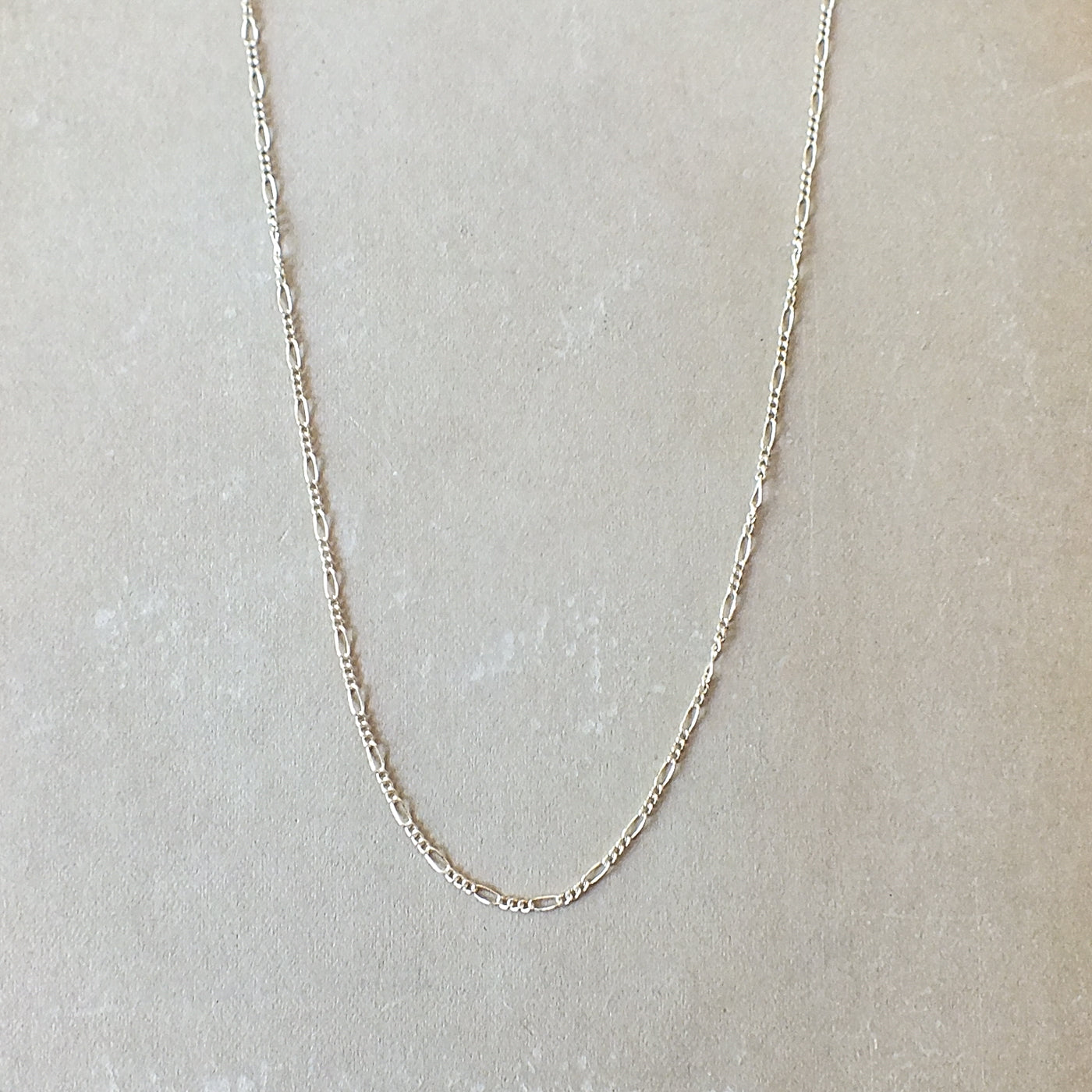 Gold filled Becoming Jewelry Figaro chain necklace on a textured grey background.