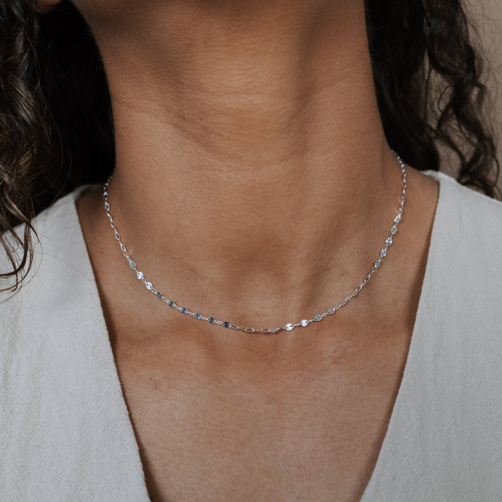 Close-up of a person wearing a delicate silver necklace against a neutral background