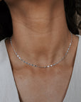 Close-up of a person wearing a delicate silver necklace against a neutral background