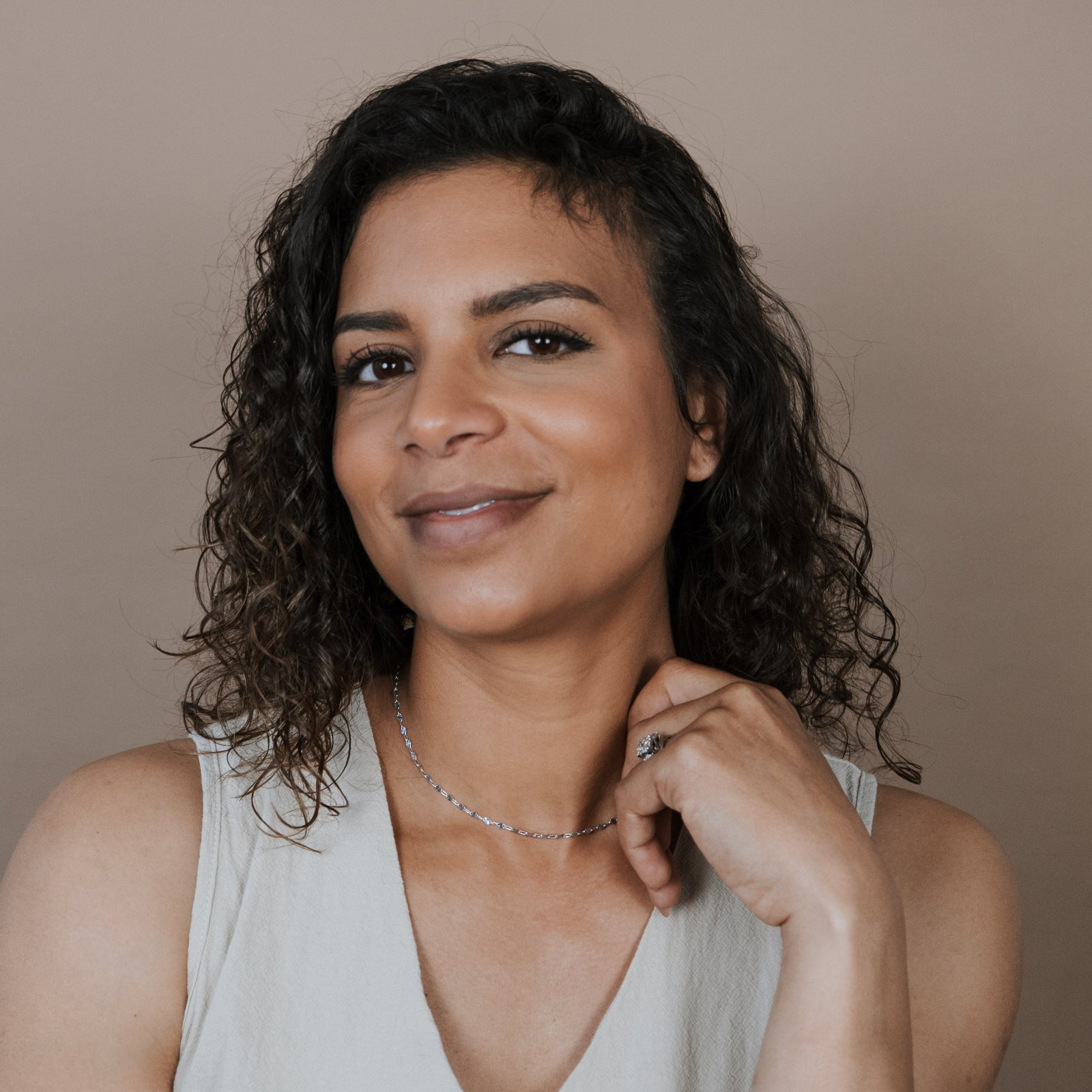 Woman wearing a starburst chain necklace and a beige sleeveless top against a plain background