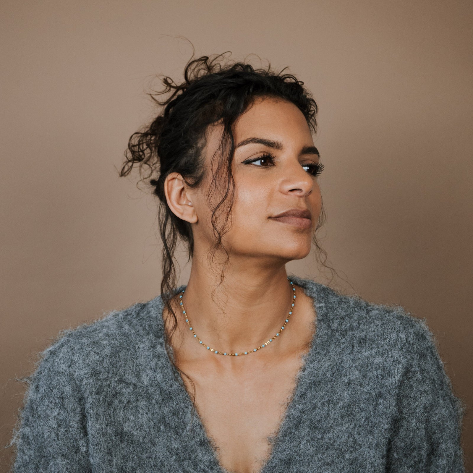 Woman wearing a gray sweater and turquoise beaded necklace against a beige background