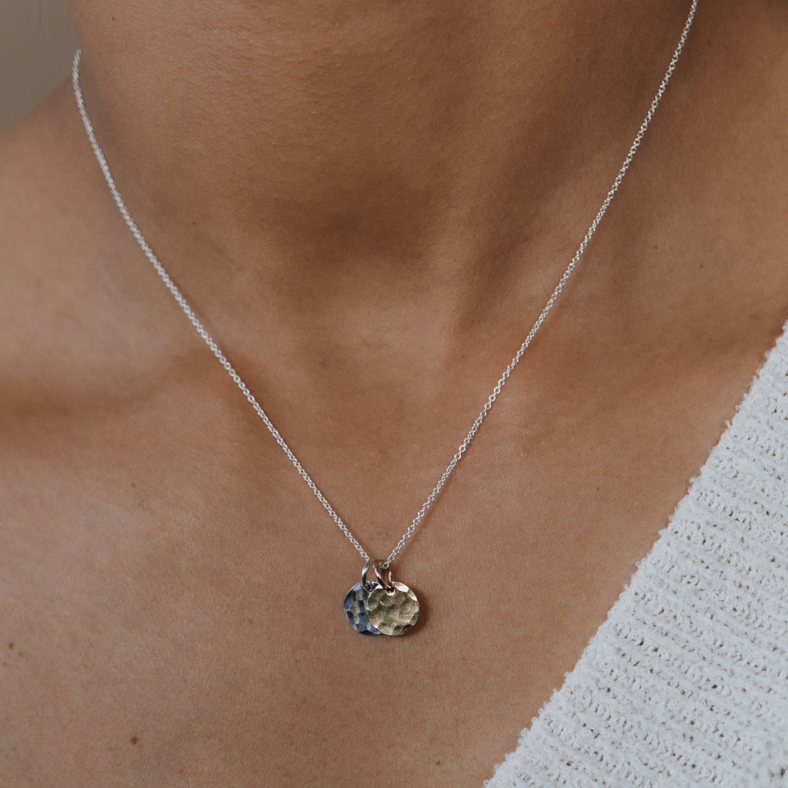 Necklace with a pendant worn by a person in a white sweater.