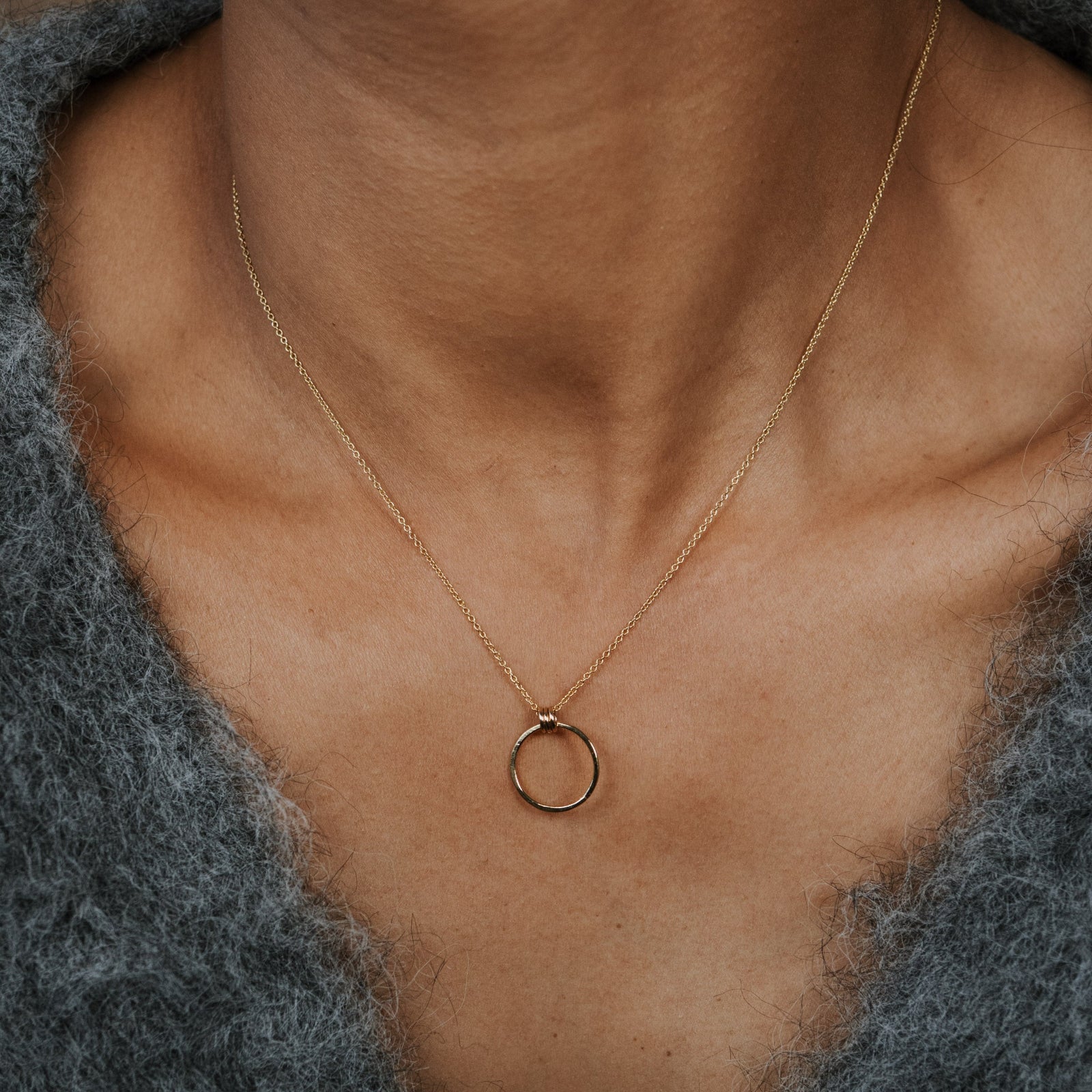 Gold necklace with a small ring pendant on a person wearing a gray sweater.