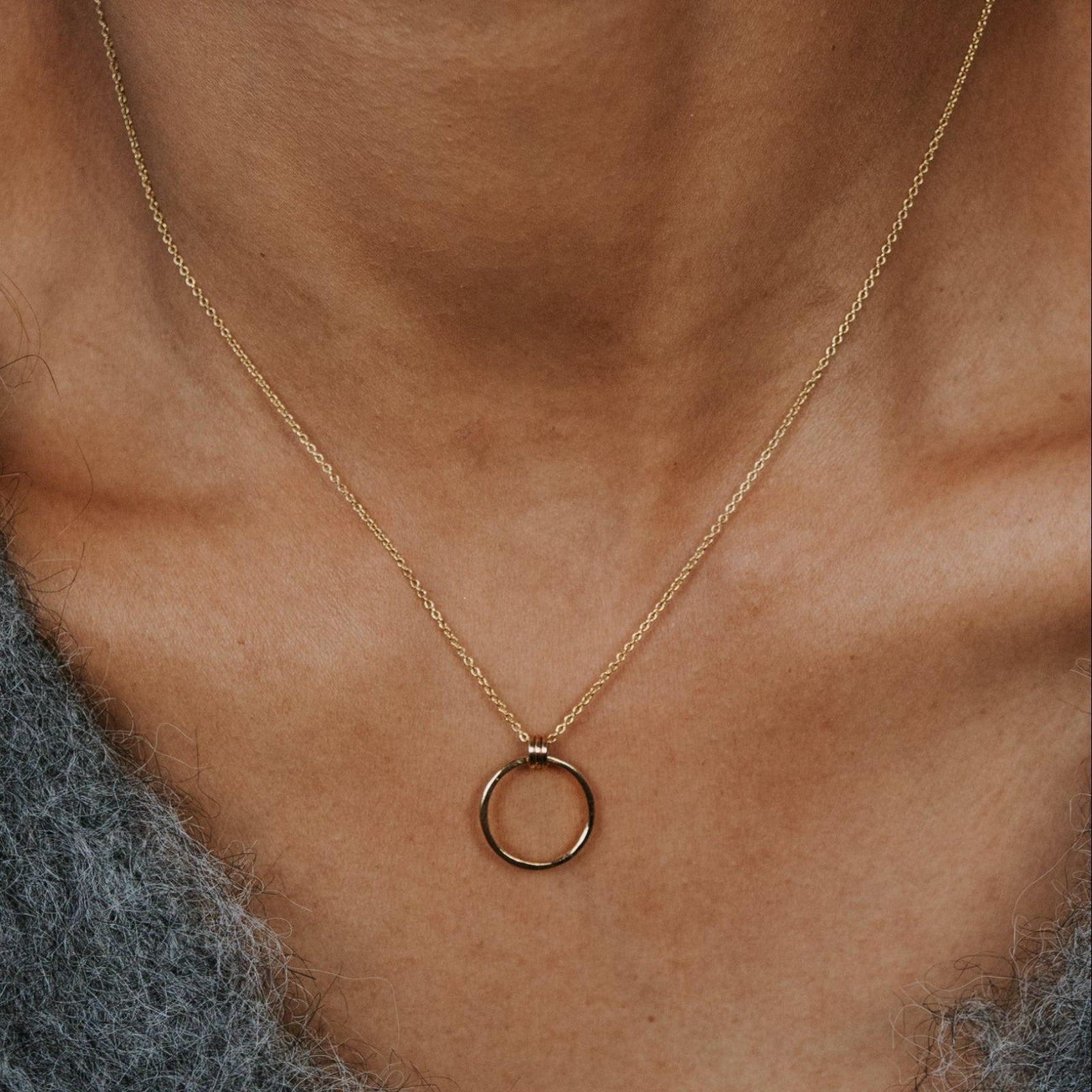 Gold necklace with a circular pendant on a person's neck