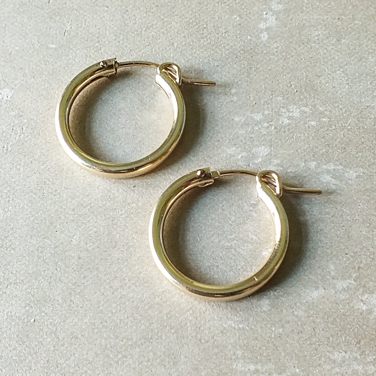 A pair of Becoming Jewelry Everyday Hoop Earrings, large on a gray surface.