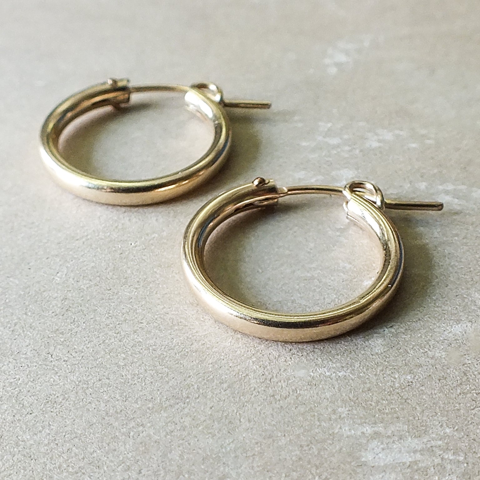 A pair of Becoming Jewelry Everyday Hoop Earrings, large on a gray surface.