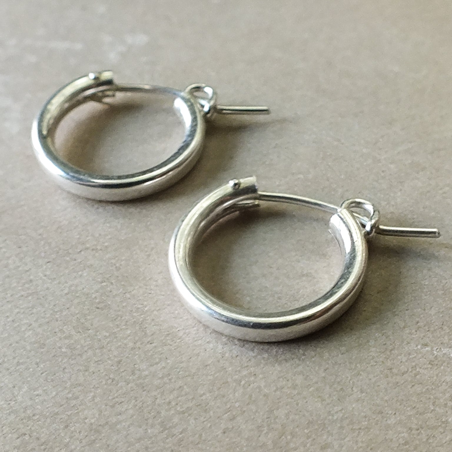 A pair of Becoming Jewelry Everyday Hoop Earrings, medium on a beige surface.
