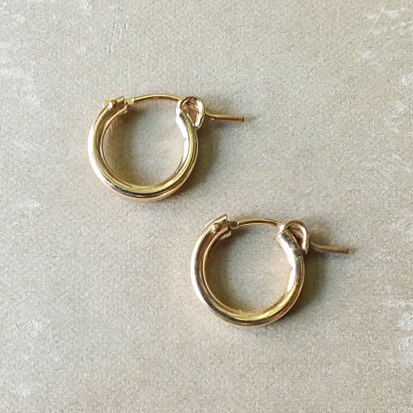 A pair of Becoming Jewelry Everyday Hoop Earrings, small on a grey surface.