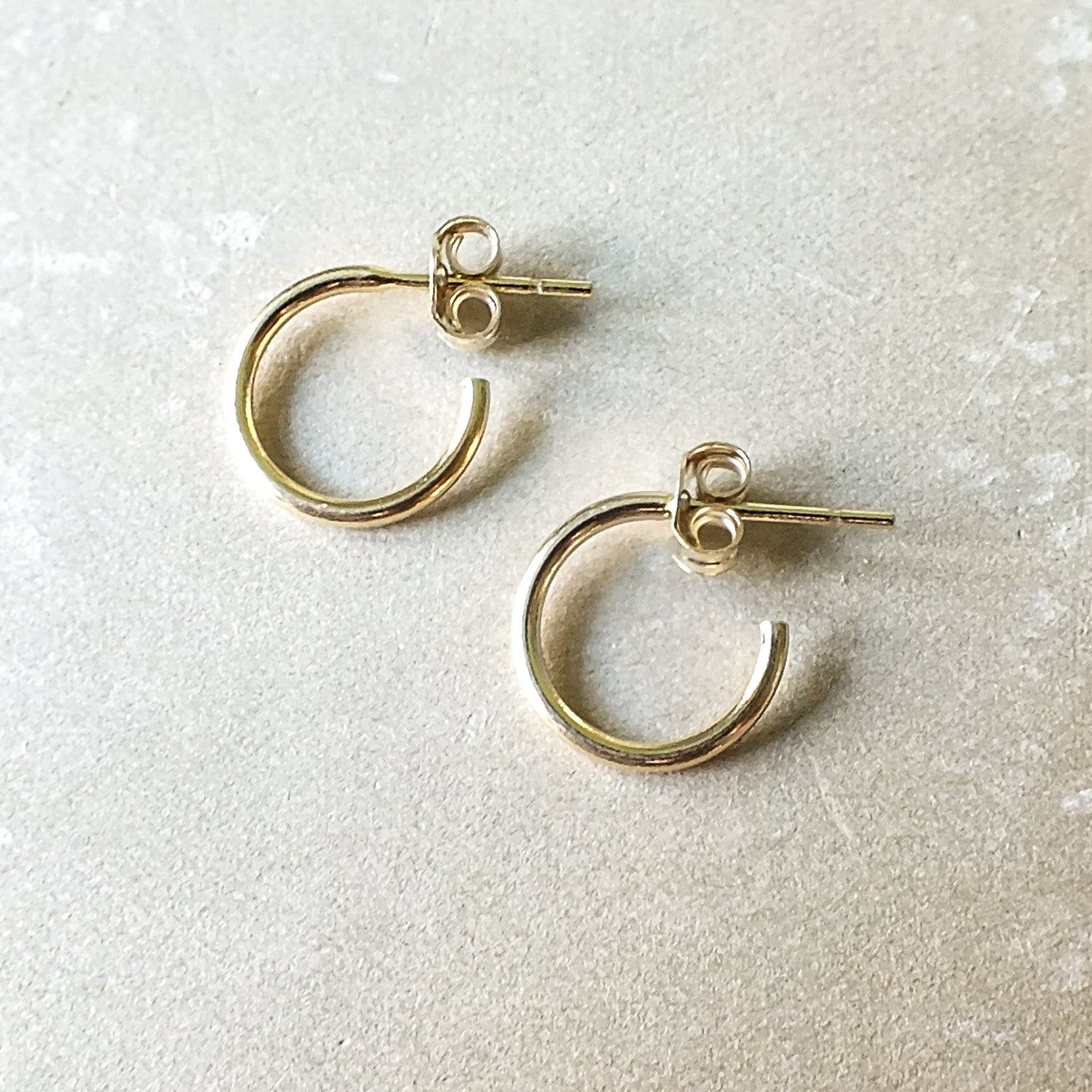 Dainty gold Open Hoop Earrings, small by Becoming Jewelry lying on a textured surface.