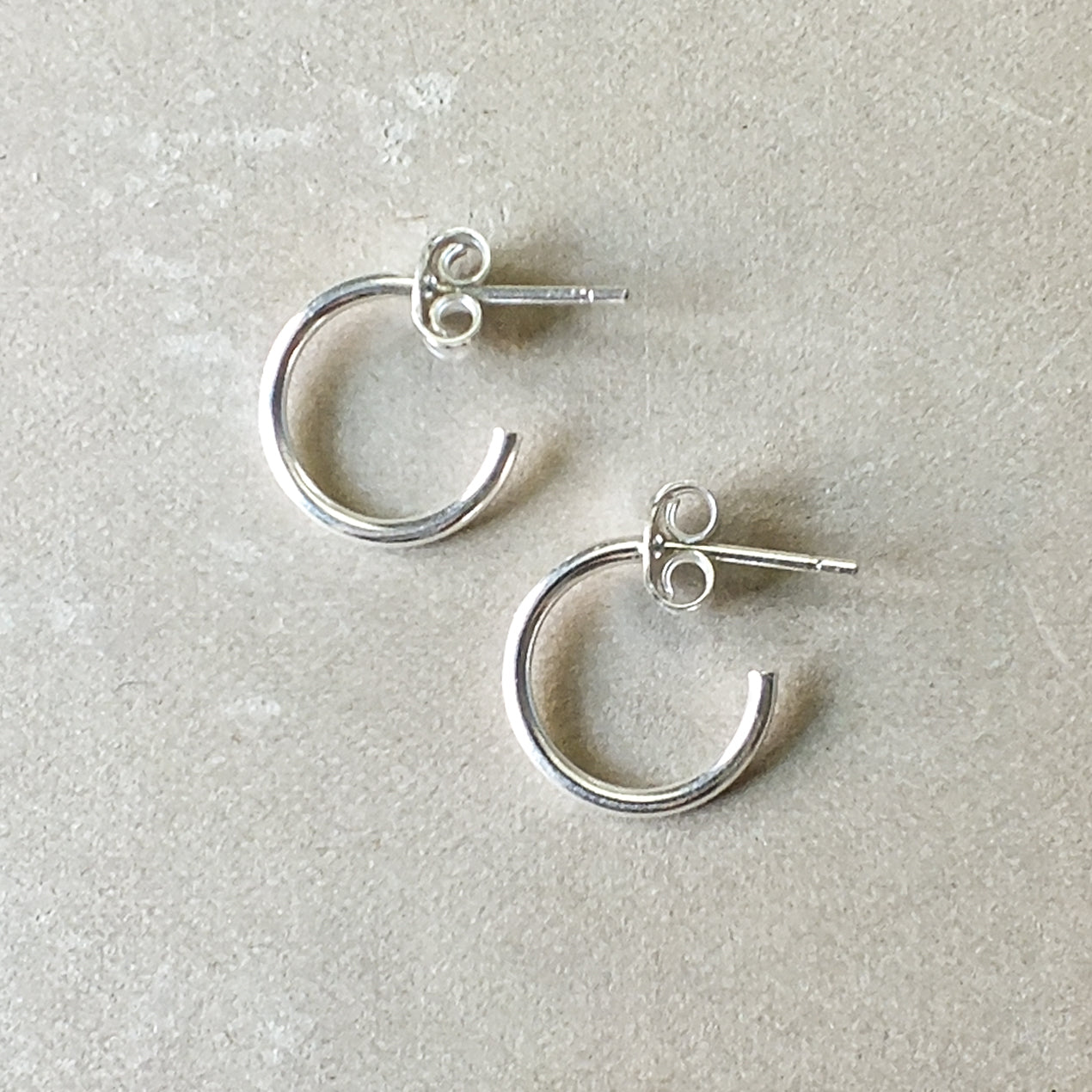 A pair of silver Open Hoop Earrings, small by Becoming Jewelry, delicately placed on a neutral textured surface.