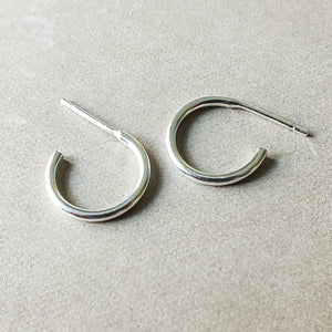 A pair of dainty, Becoming Jewelry Open Hoop Earrings, small on a beige surface.
