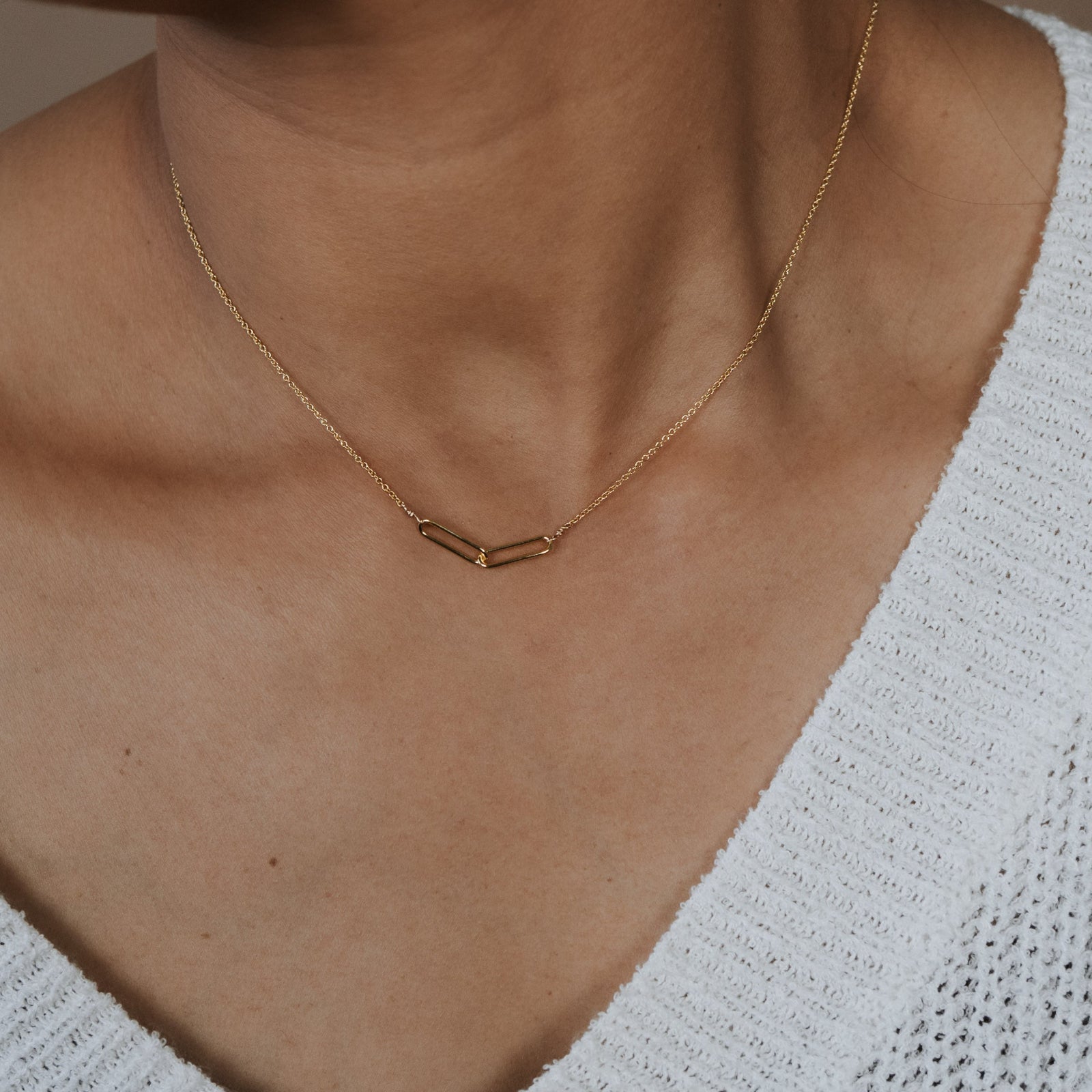 Necklace with geometric pendant on a person wearing a white sweater.