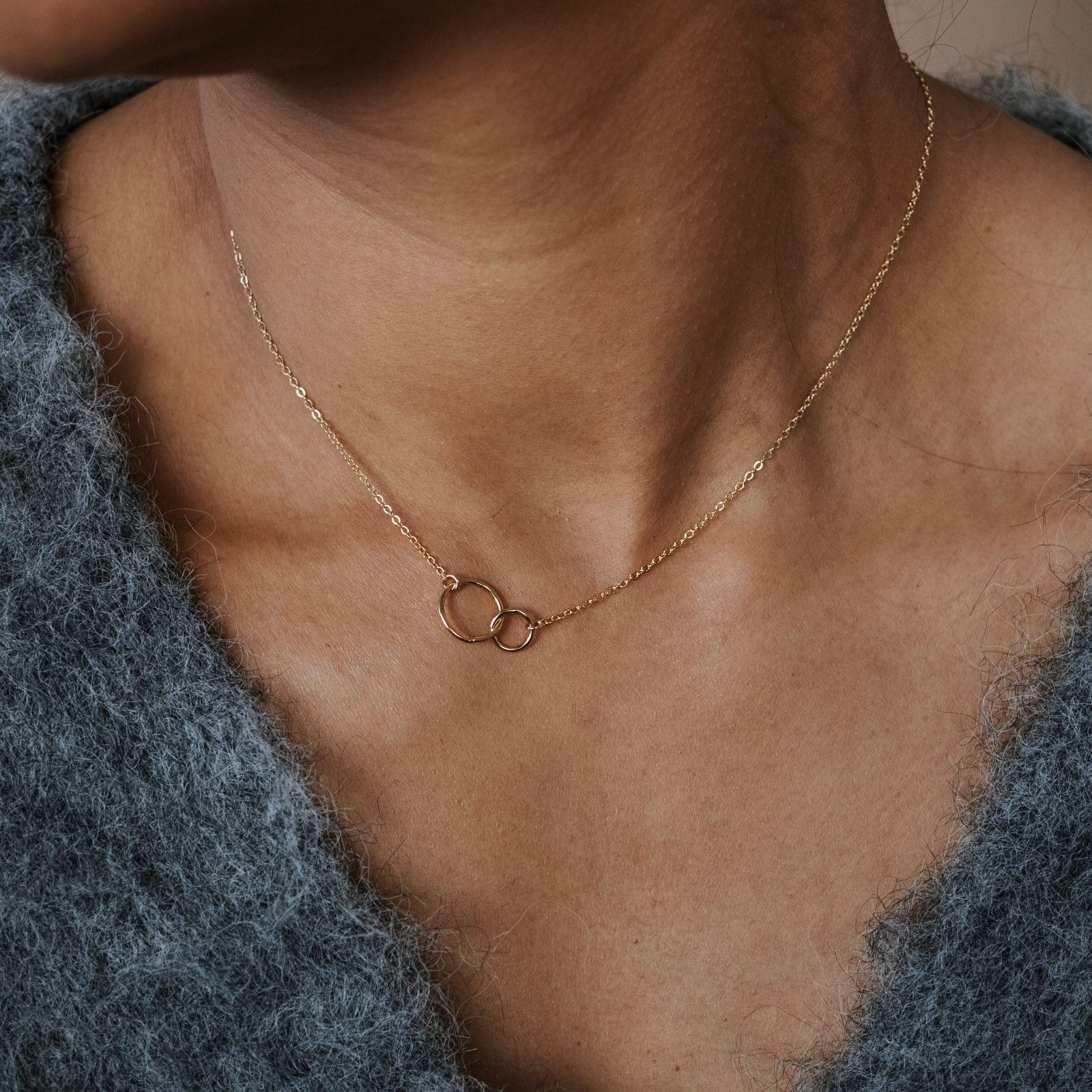 Necklace with a delicate pendant worn by a person in a textured garment.
