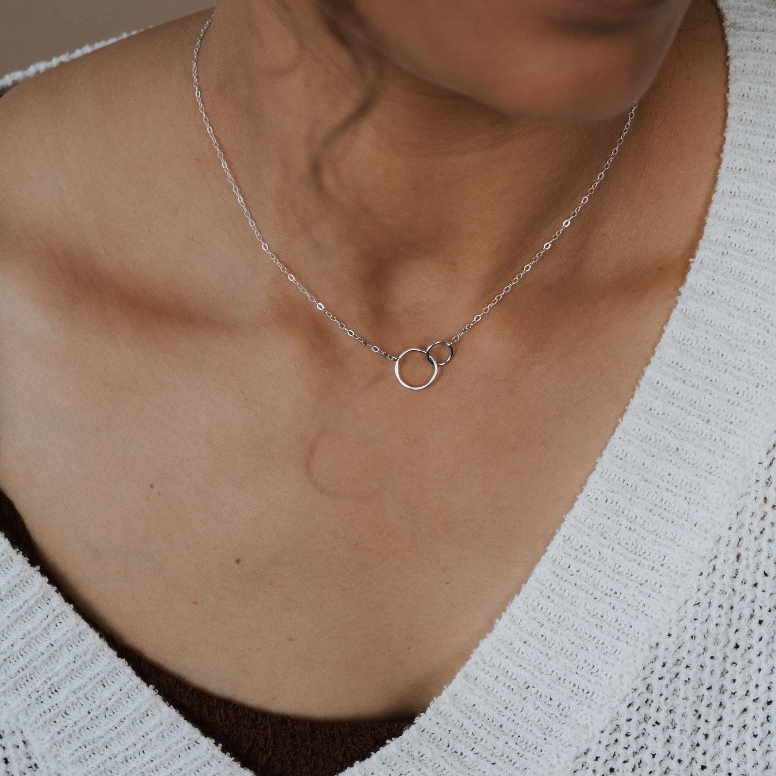 Necklace with a circular pendant worn by a person in a white sweater.