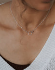 Necklace with a circular pendant worn by a person in a white sweater.