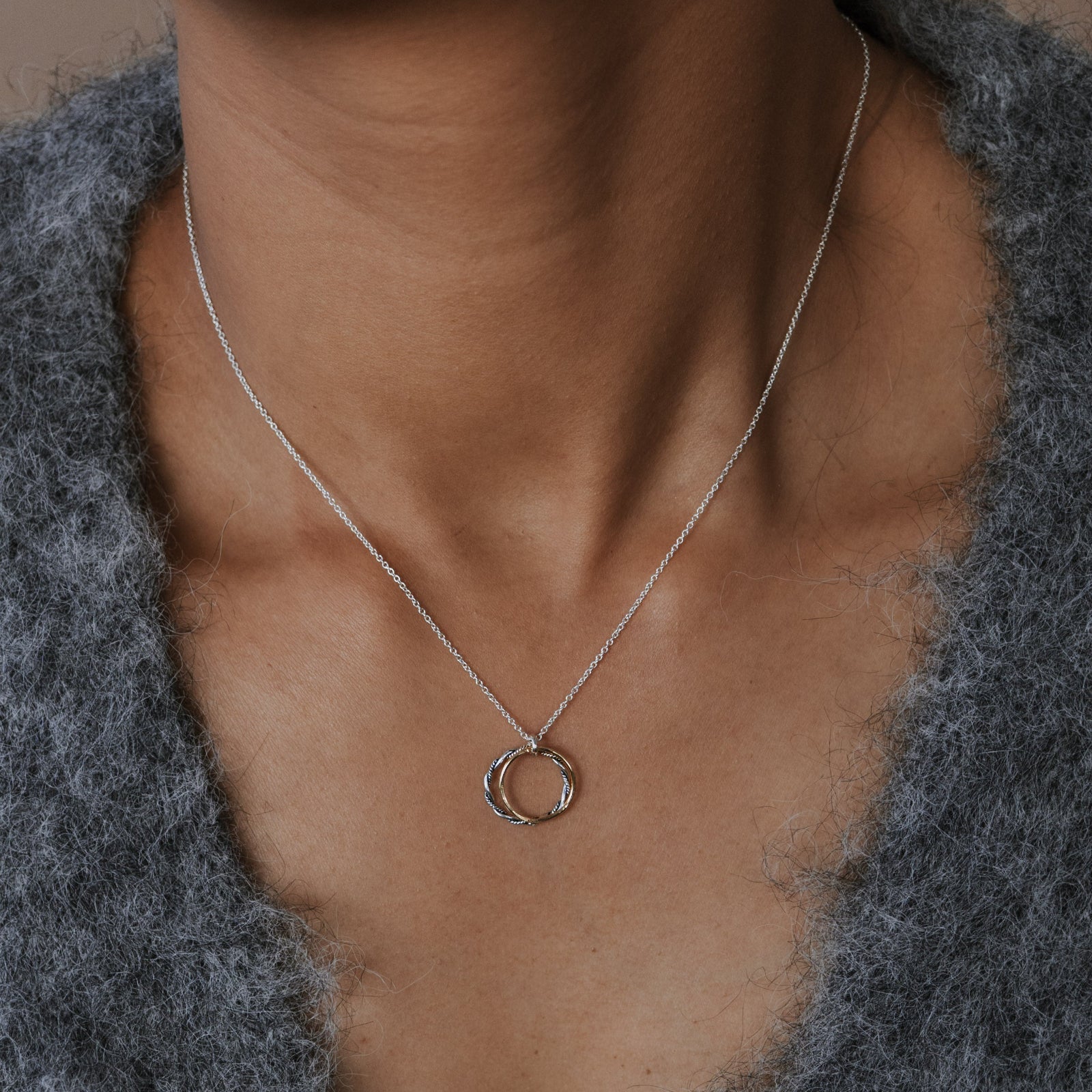 Necklace with a circular pendant worn by a person in a gray sweater.
