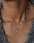 Necklace with a circular pendant worn by a person in a gray sweater.