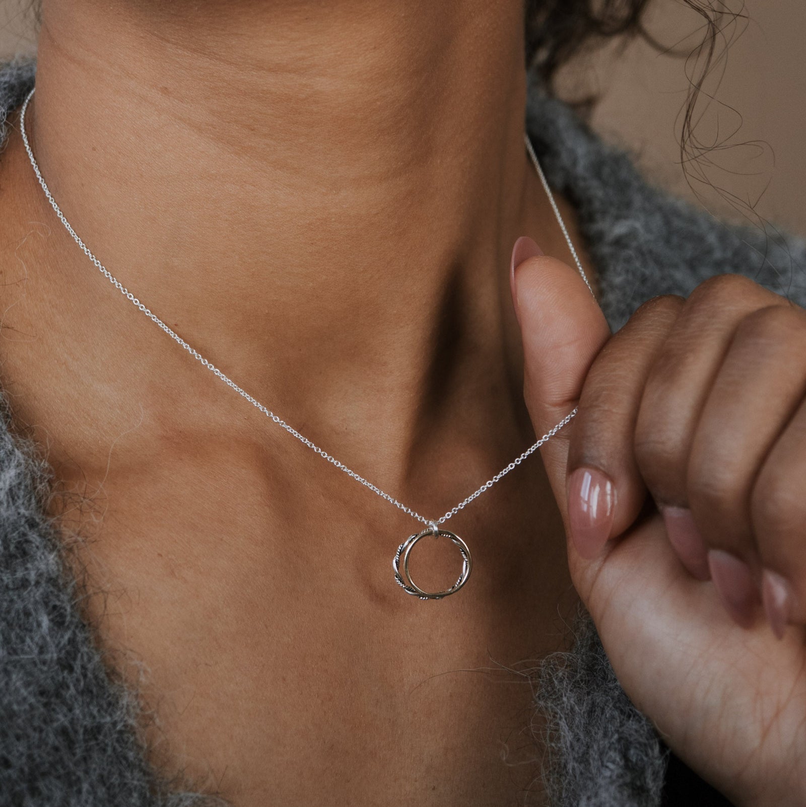 Person wearing a silver necklace with a small pendant, holding it near their neck.