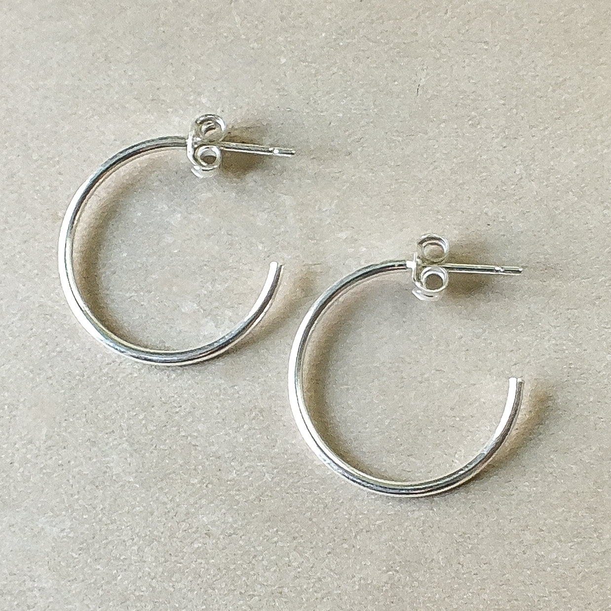 A pair of large, lightweight silver Open Hoop Earrings from Becoming Jewelry, laying on a beige surface, perfect for those who appreciate dainty jewelry.