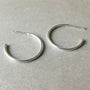 A pair of Open Hoop Earrings, large by Becoming Jewelry, embodying the elegance of dainty jewelry, is placed on a smooth, light-colored surface.