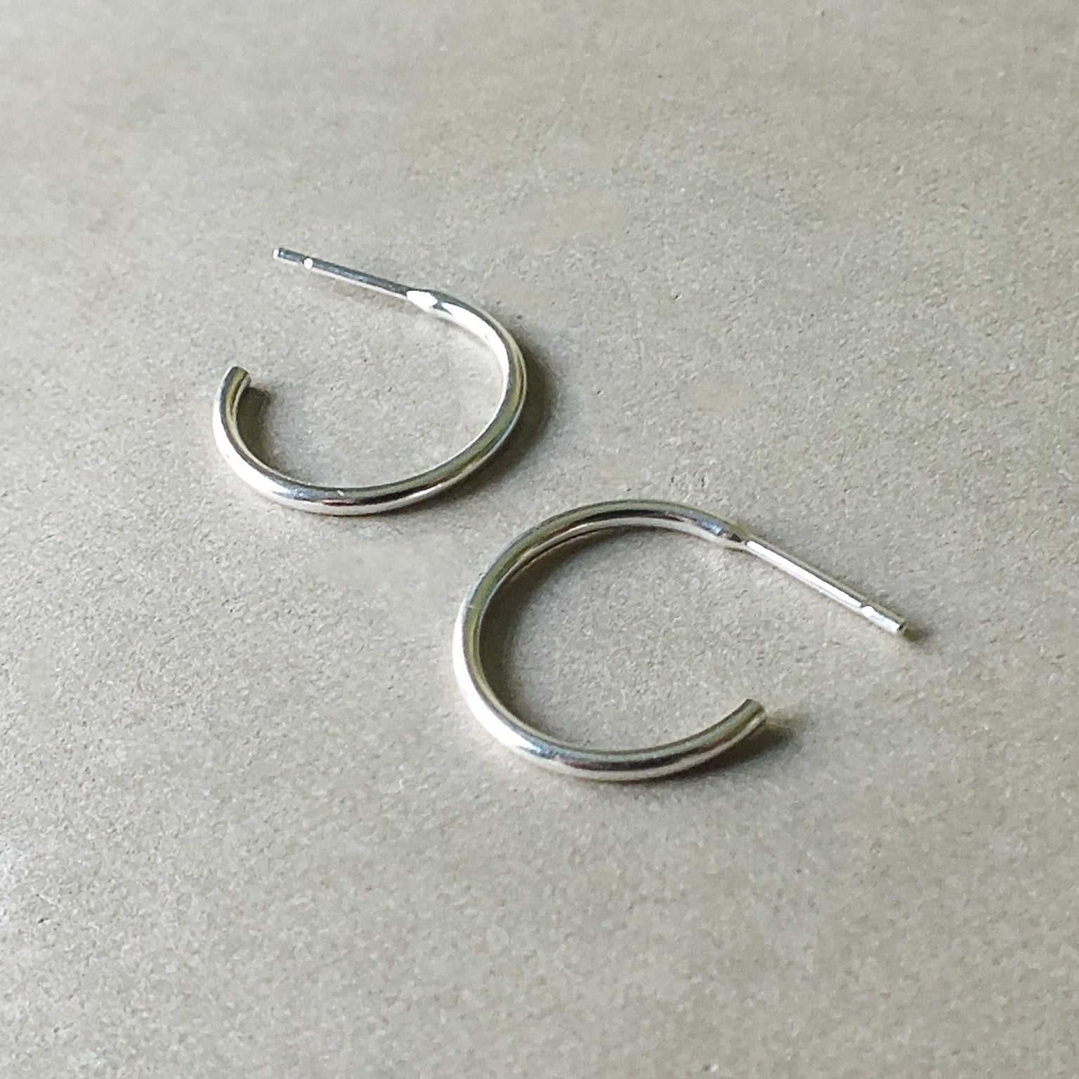 Two Becoming Jewelry medium Open Hoop Earrings in sterling silver on a gray surface.