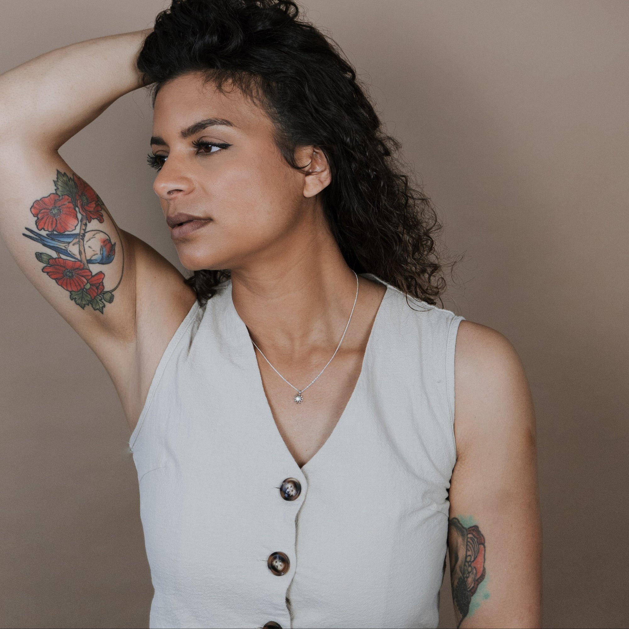 Woman with tattoos and a sleeveless top against a plain background