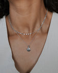 Close-up of a person wearing a silver necklace with a pendant against a neutral background