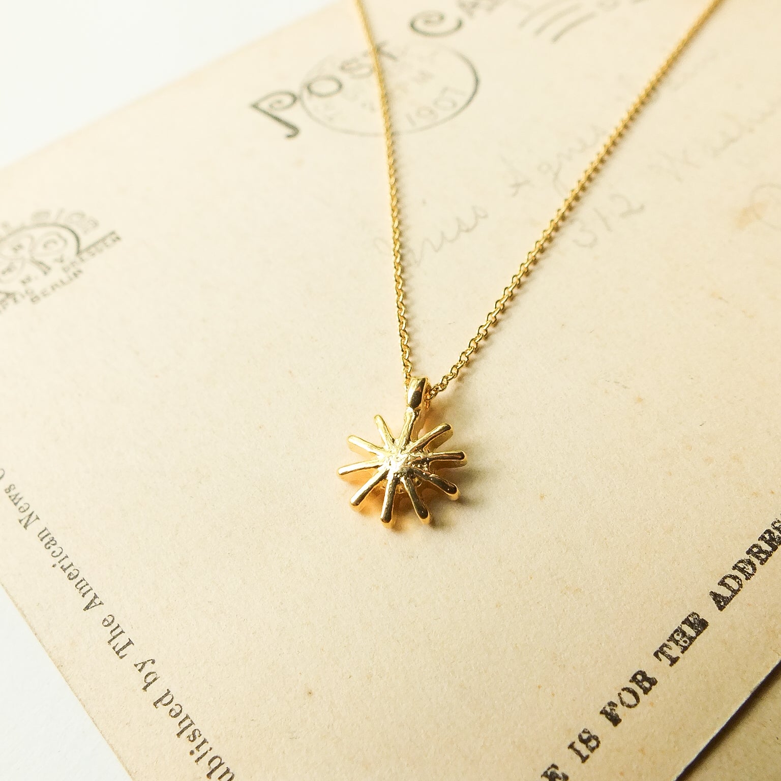 Gold necklace with a sun-shaped pendant on a textured card