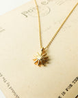 Gold necklace with a sun-shaped pendant on a textured card
