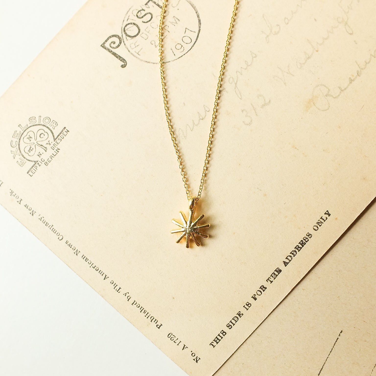 Gold necklace with a sun-shaped pendant on an old postcard background