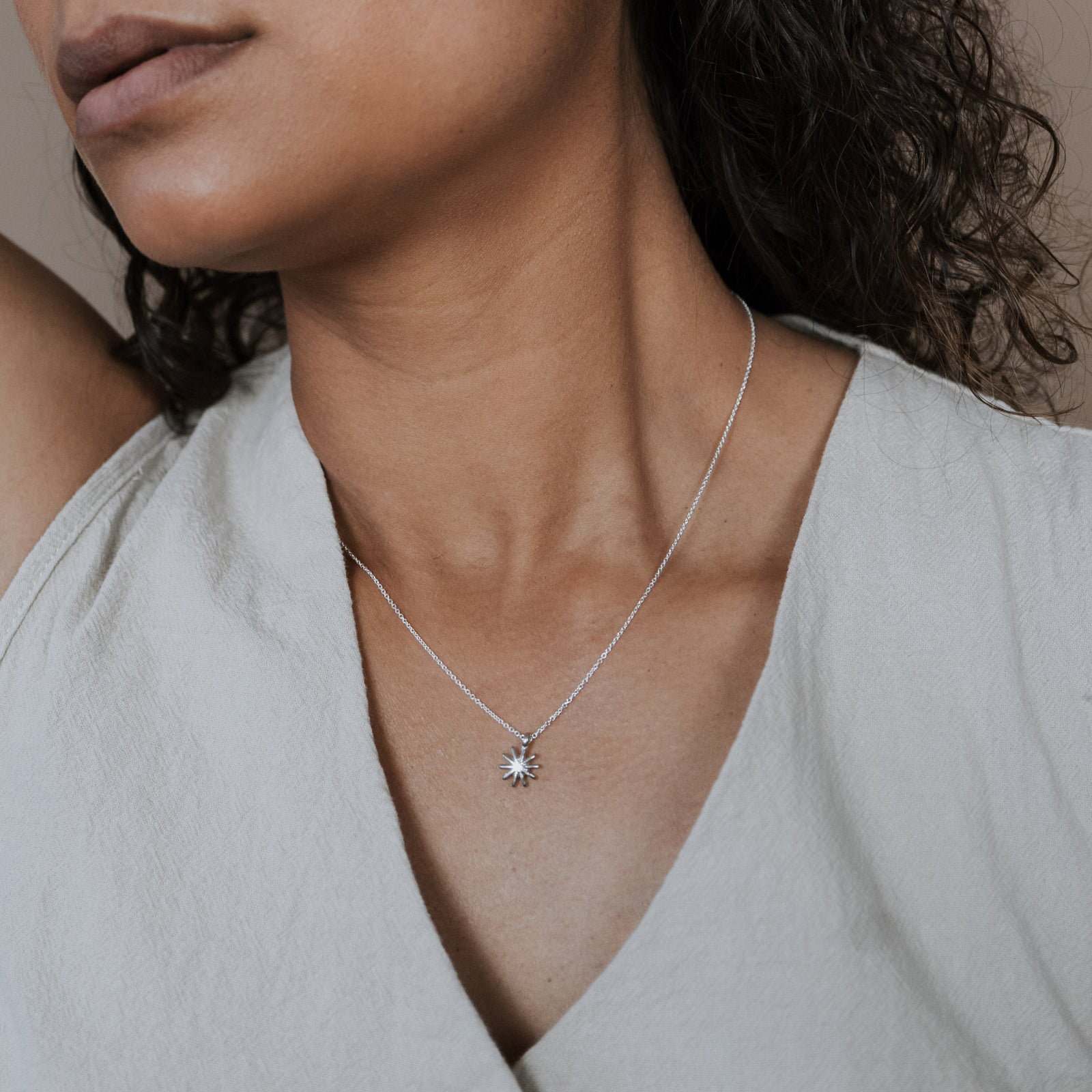 Woman wearing a silver necklace with a sunshine charm against a neutral background