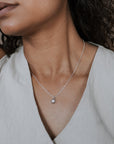 Woman wearing a silver necklace with a sunshine charm against a neutral background