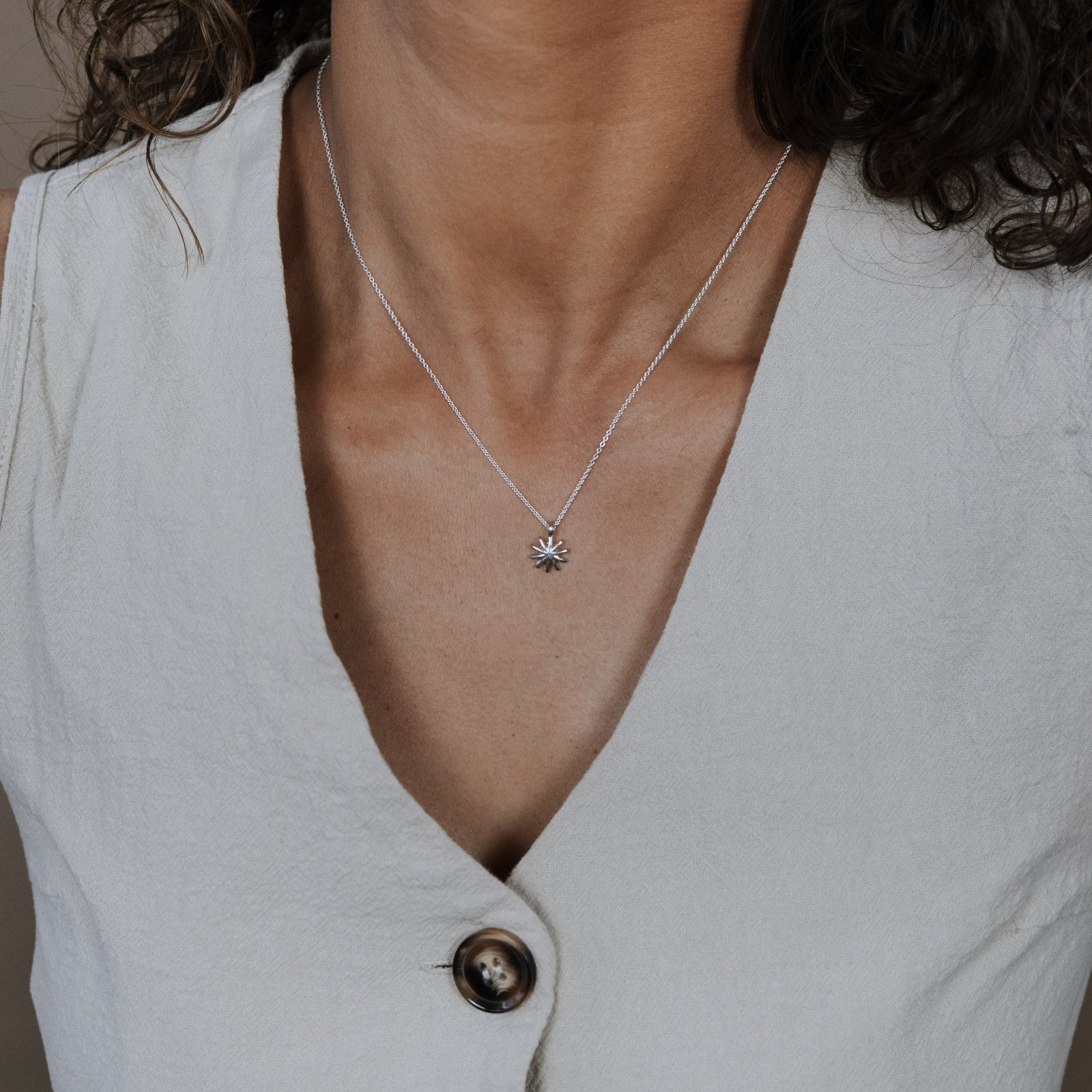 Person wearing a light gray sleeveless top with a necklace featuring a sunshine charm.