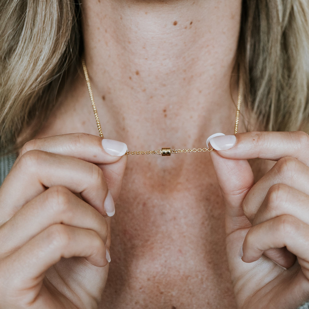 Someone holding a delicate Stick Together Necklace from Becoming Jewelry with both hands, highlighting the small barrel clasp at the center.