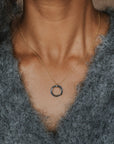 A close-up of a person wearing a delicate gold chain necklace with a small circular ring pendant, styled with a fuzzy gray button-up sweater.