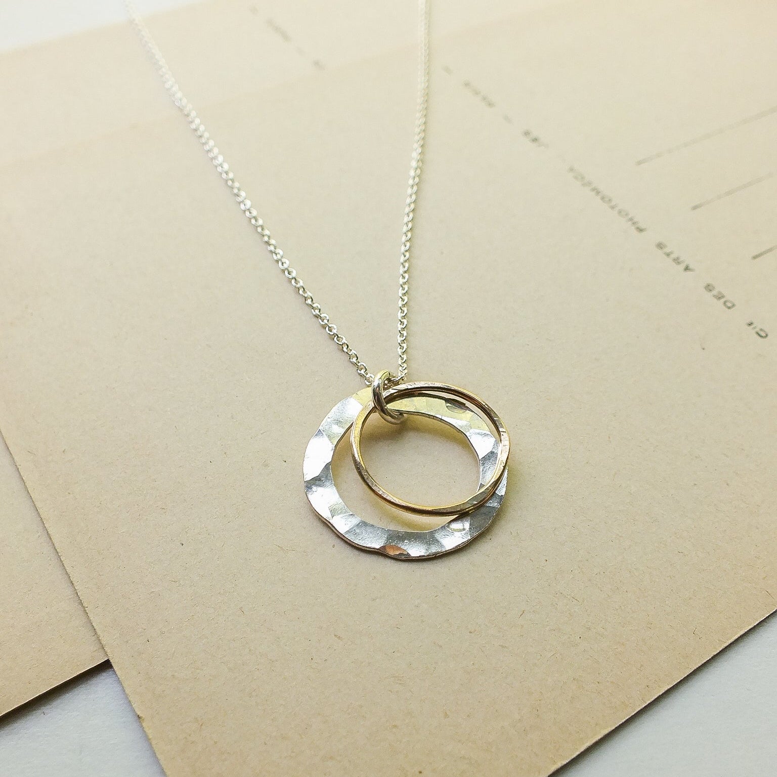 Necklace with a gold and silver circular pendant on a beige card.