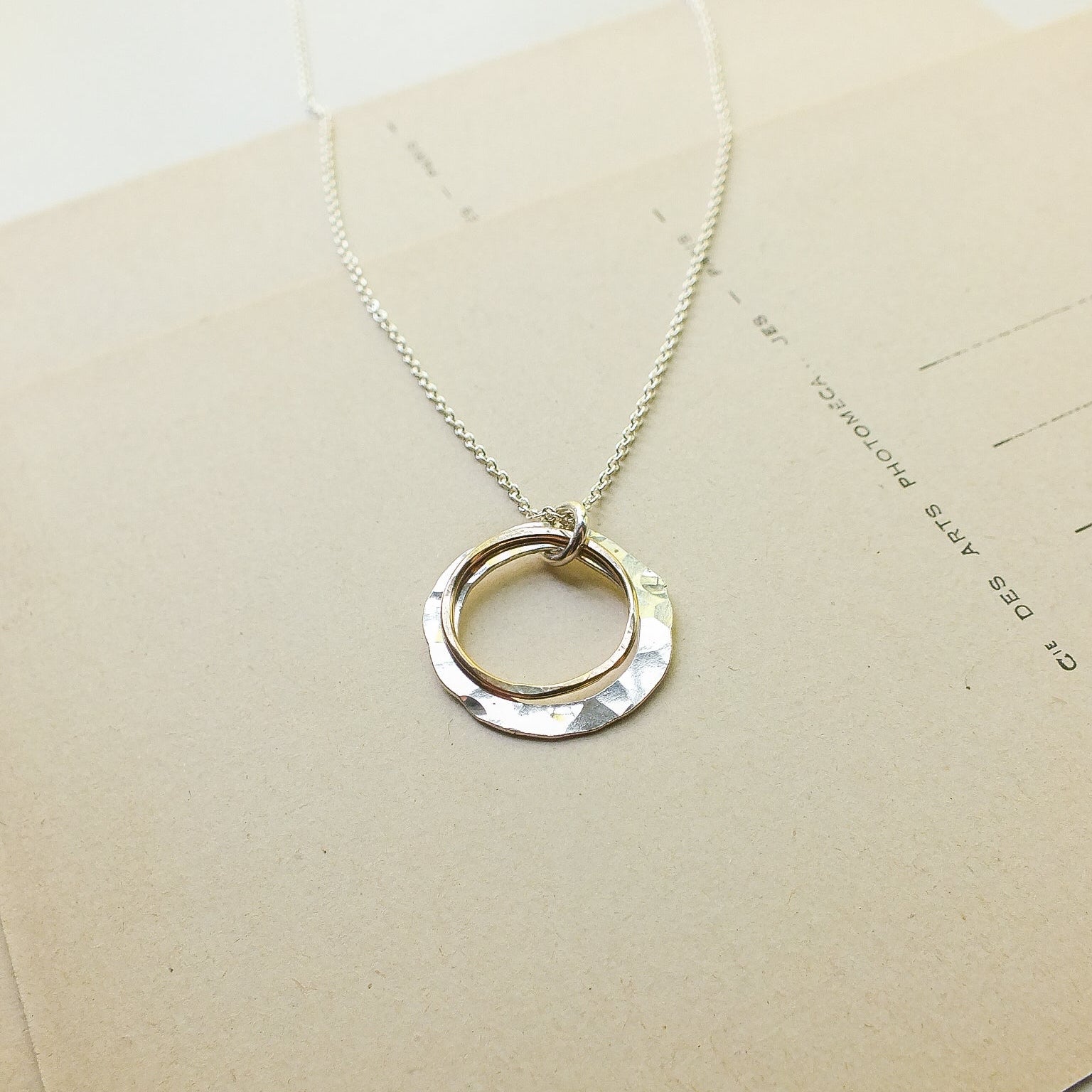 Silver necklace with a circular pendant on a beige card