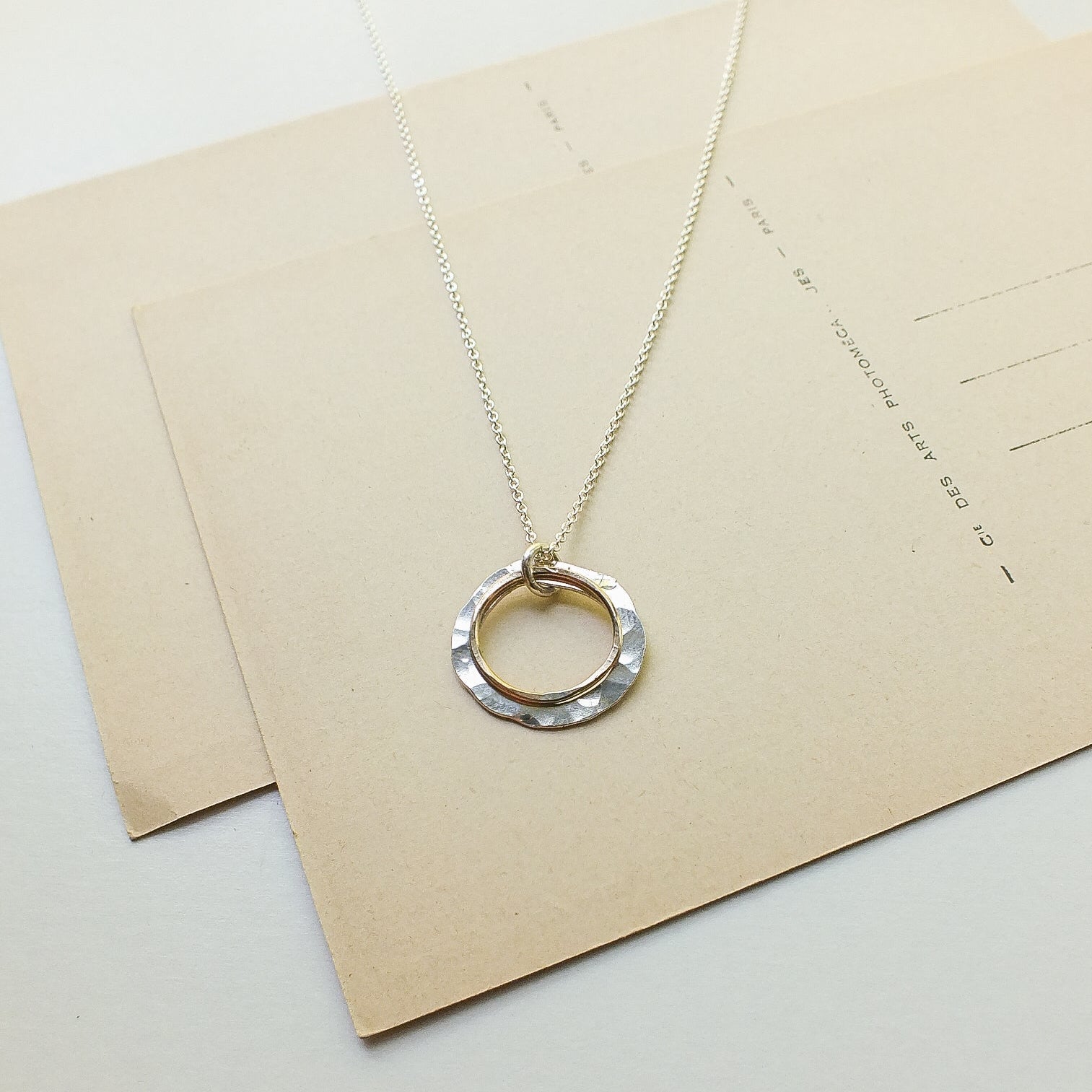Silver necklace with a circular pendant on a beige envelope