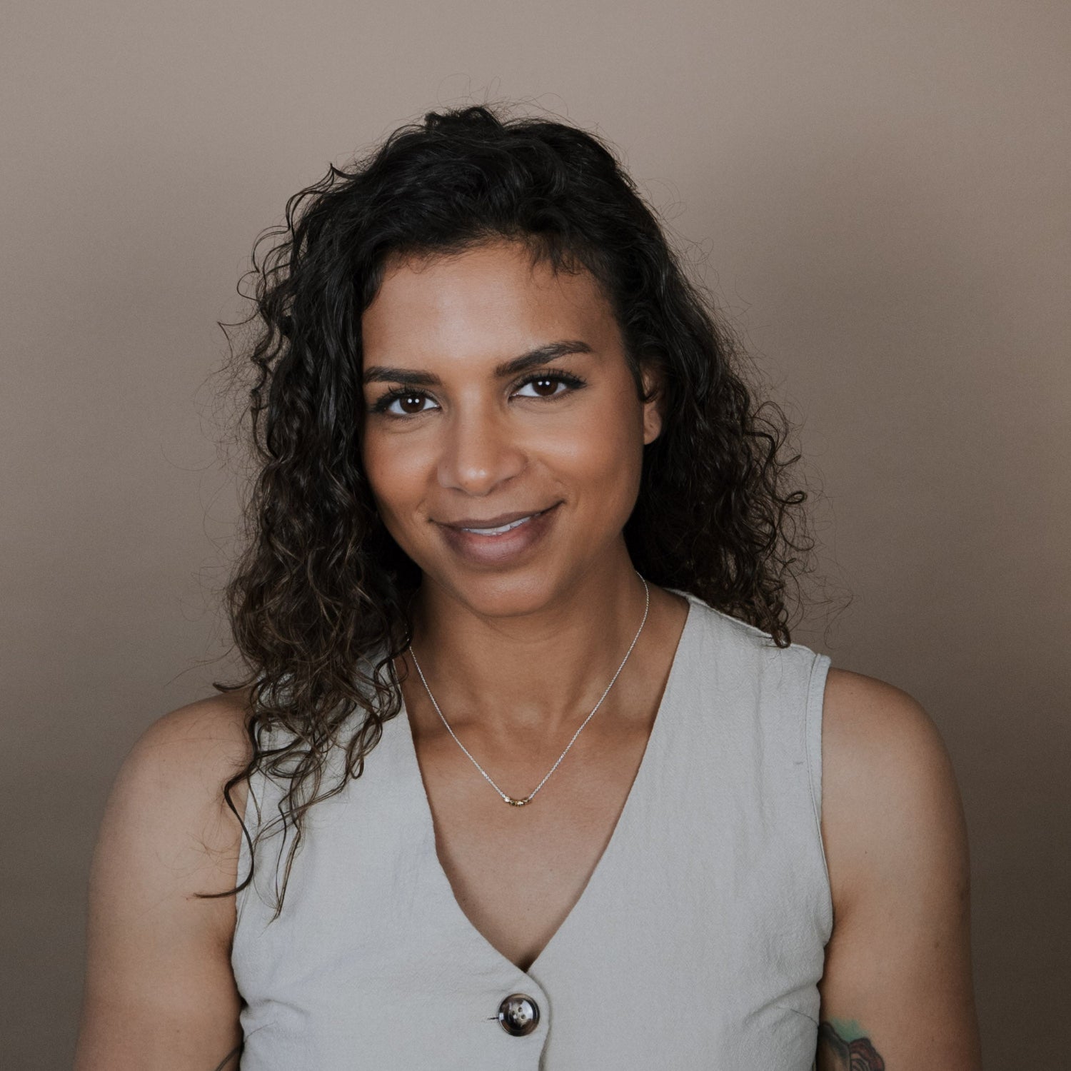 Woman wearing a light gray sleeveless top with buttons against a plain background