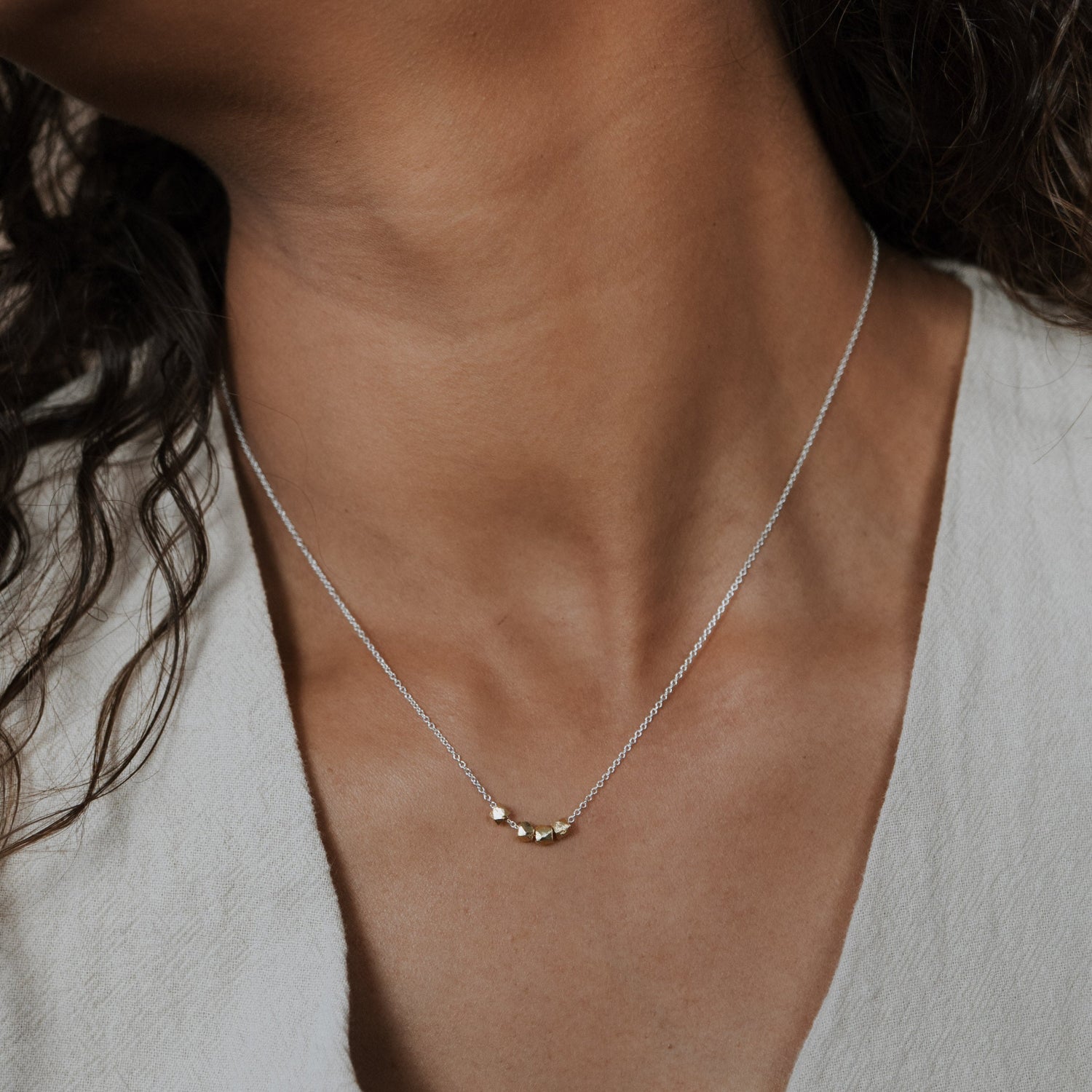 Necklace with a small pendant worn by a person in a light-colored top.