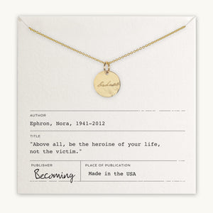 A Badass Necklace by Becoming Jewelry with the word "becoming" engraved, displayed on a card featuring a quote by Nora Ephron, "Above all, be the heroine of your life, not the victim".