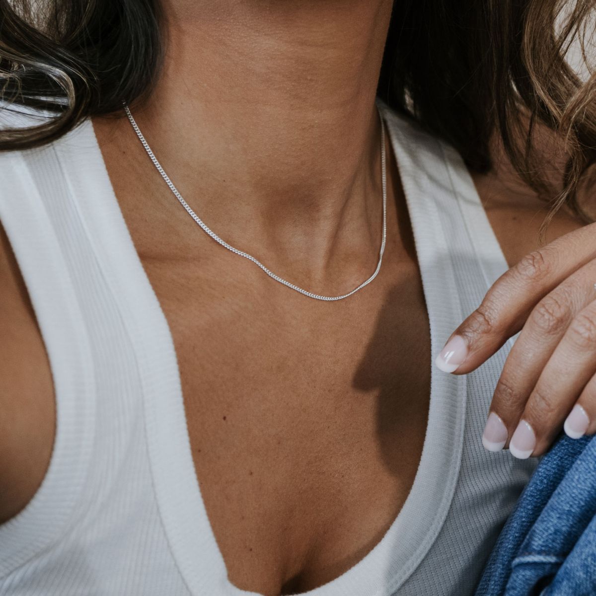 Close-up of someone in a white tank top wearing Becoming Jewelrys Curb Chain Necklace, with fingers resting on the collar.