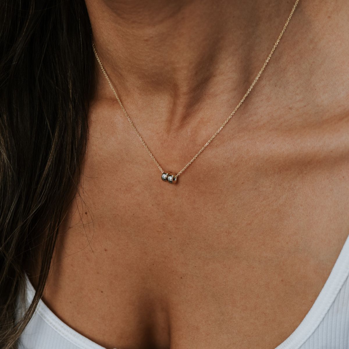 A person wearing the Friends Beads Necklace by Becoming Jewelry over a white tank top. This elegant, thin gold necklace with a small pendant and round beads is perfect for celebrating friendship, capturing the essence of cherished bonds in its simple yet sophisticated design.