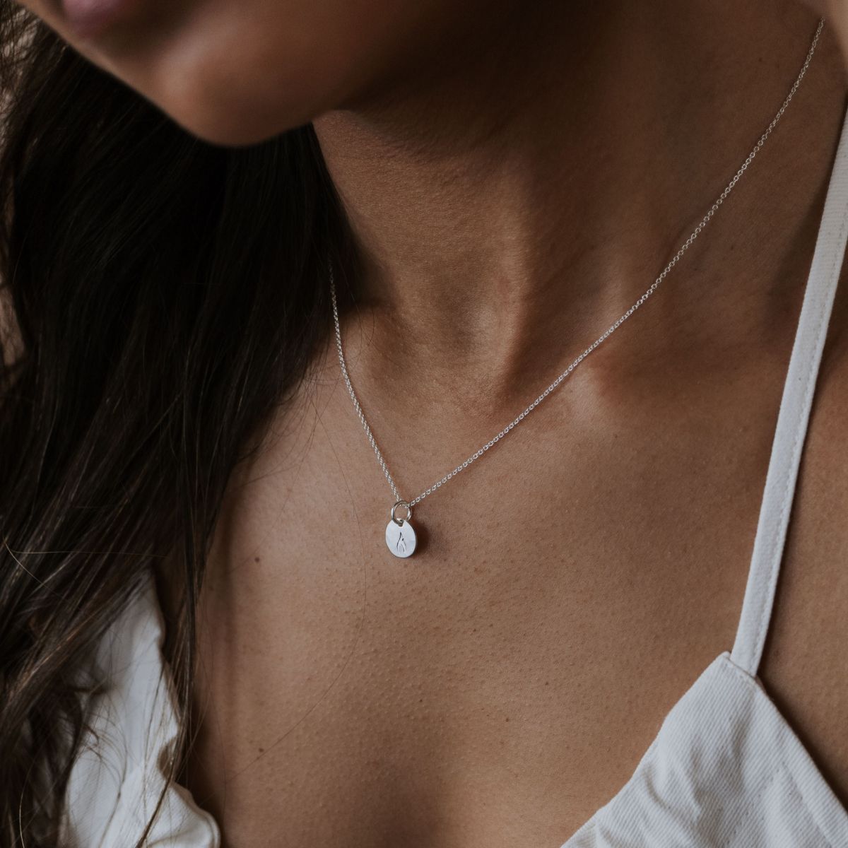 A person wearing a Becoming Jewelrys On Fire Necklace with a small round B pendant exudes passion and motivation, dressed in a light-colored top.