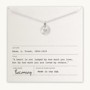 Silver heart charm pendant on a chain displayed on a card with an inspirational quote by L. Frank Baum from Becoming Jewelry's Heart Necklace.