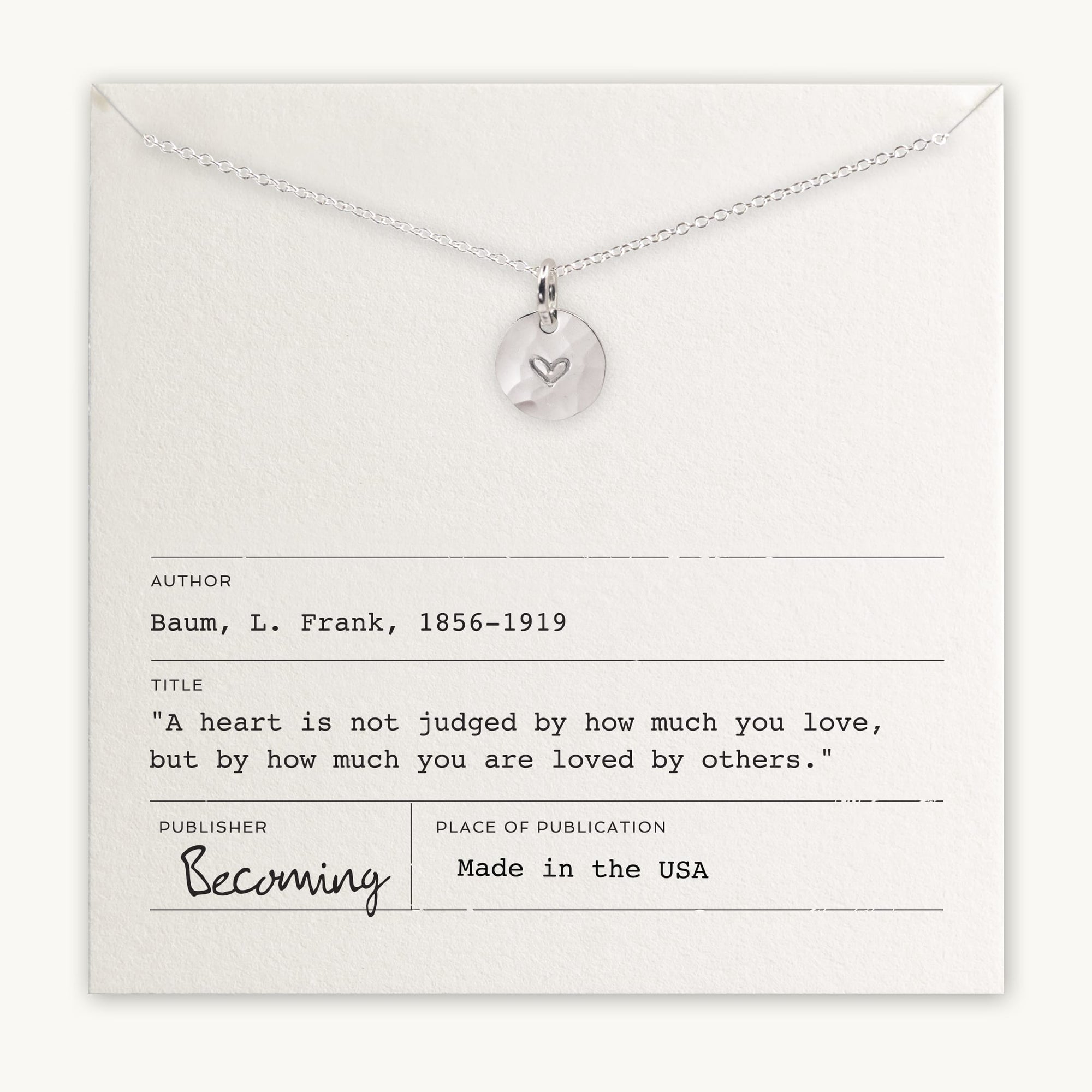 Silver heart charm pendant on a chain displayed on a card with an inspirational quote by L. Frank Baum from Becoming Jewelry's Heart Necklace.