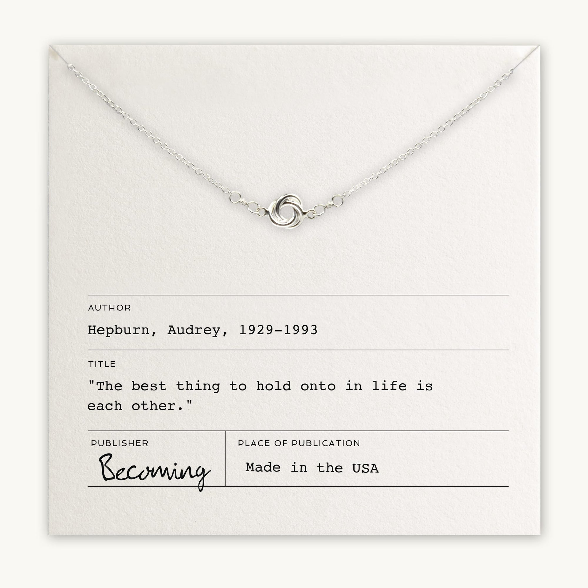 A Love Knot Necklace laid over a card with a quote by Audrey Hepburn, titled &quot;Becoming,&quot; made in the USA by Becoming Jewelry.